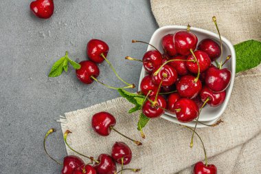 Taze nane yapraklı olgun kirazlar, geleneksel yaz meyveleri. Modaya uygun beton standları, kaliteli peçeteler. Gri taş arkaplan, üst manzara
