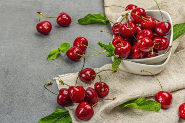 Taze nane yapraklı olgun kirazlar, geleneksel yaz meyveleri. Modaya uygun beton standları, kaliteli peçeteler. Gri taş beton zemin, kopyalama alanı