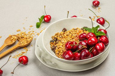 Yaz kahvaltısı kavramı. Sağlıklı sabah yemeği. Olgun kiraz ve granola, hafif beton arka plan, düz yatış, yakın çekim