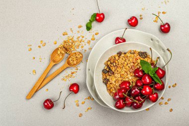 Summer breakfast concept. Healthy morning food. Ripe cherries and granola, light concrete background, flat lay, top view