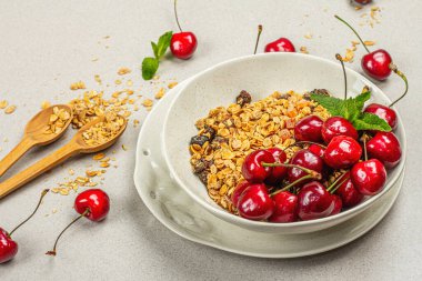 Yaz kahvaltısı kavramı. Sağlıklı sabah yemeği. Olgun kiraz ve granola, hafif beton arka plan, düz yatış, yakın çekim