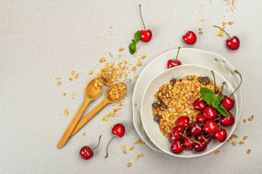 Yaz kahvaltısı kavramı. Sağlıklı sabah yemeği. Olgun kiraz ve granola, açık beton zemin, düz yatış, üst manzara