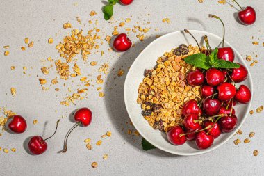 Yaz kahvaltısı kavramı. Sağlıklı sabah yemeği. Olgun kiraz ve tahıl gevreği, açık beton arka plan, düz yatak. Modaya uygun sert ışık, koyu gölge, üst manzara