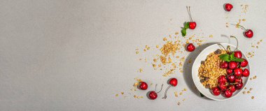 Summer breakfast concept. Healthy morning food. Ripe cherries and granola, light concrete background, flat lay. Trendy hard light, dark shadow, banner format