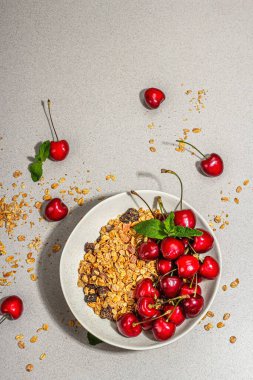 Summer breakfast concept. Healthy morning food. Ripe cherries and granola, light concrete background, flat lay. Trendy hard light, dark shadow, top view