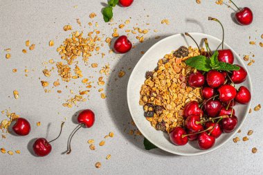 Yaz kahvaltısı kavramı. Sağlıklı sabah yemeği. Olgun kiraz ve tahıl gevreği, açık beton arka plan, düz yatak. Modaya uygun sert ışık, koyu gölge, üst manzara