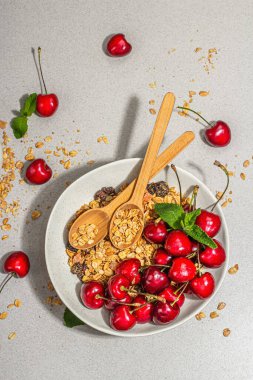 Yaz kahvaltısı kavramı. Sağlıklı sabah yemeği. Olgun kiraz ve tahıl gevreği, açık beton arka plan, düz yatak. Modaya uygun sert ışık, koyu gölge, üst manzara