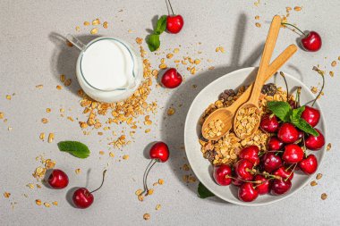 Yaz kahvaltısı kavramı. Sağlıklı sabah yemeği. Olgun kiraz ve tahıl gevreği, açık beton arka plan, düz yatak. Modaya uygun sert ışık, koyu gölge, üst manzara
