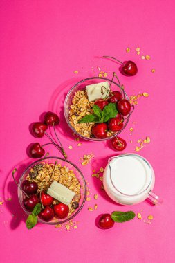 Yaz kahvaltısı kavramı. Sağlıklı sabah yemeği. Olgun kiraz, süt, beyaz çikolata ve granola. Modaya uygun bir aydınlatma, koyu gölge, pembe arka plan, üst görünüm