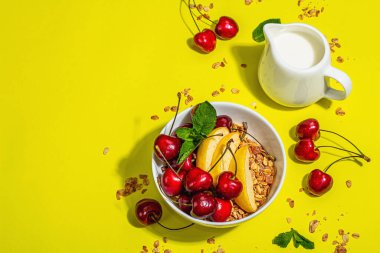 Yaz kahvaltısı kavramı. Sağlıklı sabah yemeği. Olgun kiraz, elma, süt ve tahıl gevreği. Modaya uygun bir ışık, koyu gölge, sarı arkaplan, üst görünüm