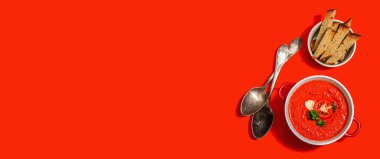 Spicy tomato soup. Healthy vegan hot dish, croutons, vintage cutlery. Bright red background, trendy hard light, dark shadow, banner format