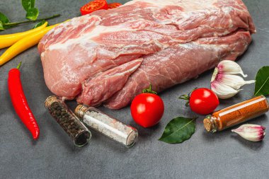 Baharatlı ve sebzeli çiğ domuz filetosu ve gri taşlı arka plan. Sağlıklı yemek, taze domates ve defne yaprağı pişirmek için geleneksel hayvan proteini. Mutfak somut konsepti, kapatın.
