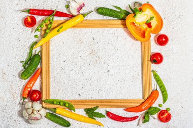 Tahta çerçevenin etrafında taze sebzeler ve baharatlar var. Olgun sarı biber, domates, bezelye, salatalık, sarımsak, renkli biber. Sağlıklı yemek pişirme, macun arka planı, üst görünüm malzemeleri.