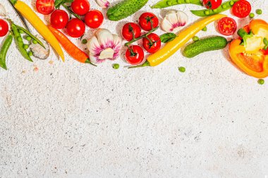 Assorted fresh vegetables and spices on light plaster background. Ripe yellow pepper, tomato, pea, cucumber, garlic, colored chilies. Ingredients for cooking healthy food, top view