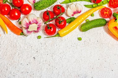 Assorted fresh vegetables and spices on light plaster background. Ripe yellow pepper, tomato, pea, cucumber, garlic, colored chilies. Ingredients for cooking healthy food, top view