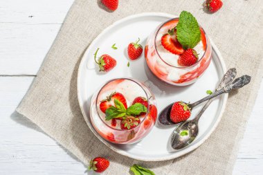 Italian dessert panna cotta in glass with strawberries. Healthy sweet food, trendy hard light, dark shadow. Rustic style concept, white wooden boards background, top view