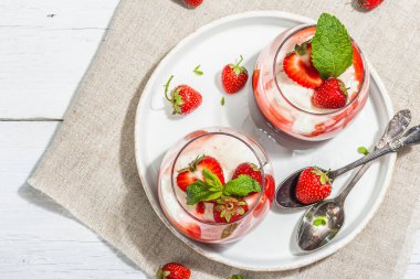 Italian dessert panna cotta in glass with strawberries. Healthy sweet food, trendy hard light, dark shadow. Rustic style concept, white wooden boards background, top view