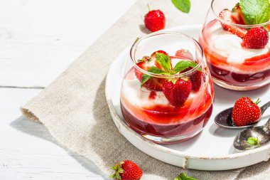 Italian dessert panna cotta in glass with strawberries. Healthy sweet food, trendy hard light, dark shadow. Rustic style concept, white wooden boards background, copy space