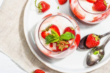 Italian dessert panna cotta in glass with strawberries. Healthy sweet food, trendy hard light, dark shadow. Rustic style concept, white wooden boards background, top view