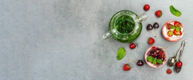 Delicious Italian dessert panna cotta with sweet cherry sauce, and strawberry jam. Mint leaves tea and fresh berries. Stone concrete background, banner format