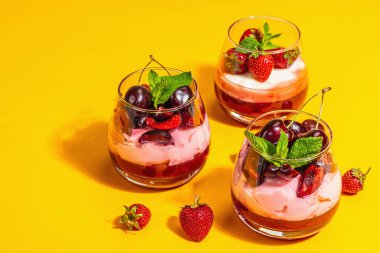 Delicious Italian dessert panna cotta with sweet cherry sauce, strawberry jam, fresh berries and mint leaves. Trendy hard light, dark shadow, bright orange background, copy space