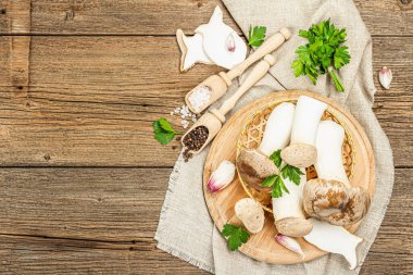 Fresh Pleurotus eryngii mushrooms on wooden background. Raw king oyster or eringi with spices and herbs. Vegan ingredient for cooking healthy food, top view