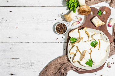 Fresh Pleurotus eryngii mushrooms on white wooden background. Raw king oyster or eringi with spices and herbs. Vegan ingredient, trendy hard light, dark shadow, top view