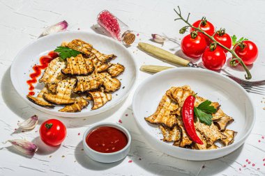 Fried slices Pleurotus eryngii mushrooms with sauce, spices and herbs. Healthy vegan food concept, hard light, dark shadowwhite plaster background, flat lay, close up