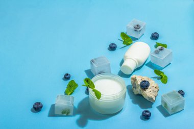 Natural skincare. Cream or lotion with organic berries. Blueberry, mint, and ice. Moisturizing and tonic cosmetics concept, flat lay, trendy hard light, dark shadow, blue background, copy space