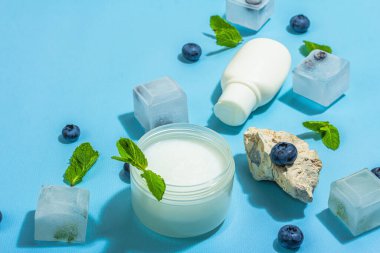 Natural skincare. Cream or lotion with organic berries. Blueberry, mint, and ice. Moisturizing and tonic cosmetics concept, flat lay, trendy hard light, dark shadow, blue background, close up