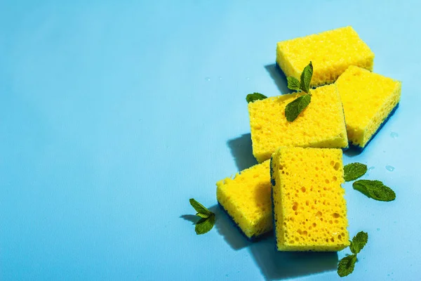 Bright yellow sponges for washing dishes. Organic cleaning concept, minty freshness. A trendy hard light, dark shadow, blue background, flat lay, copy space