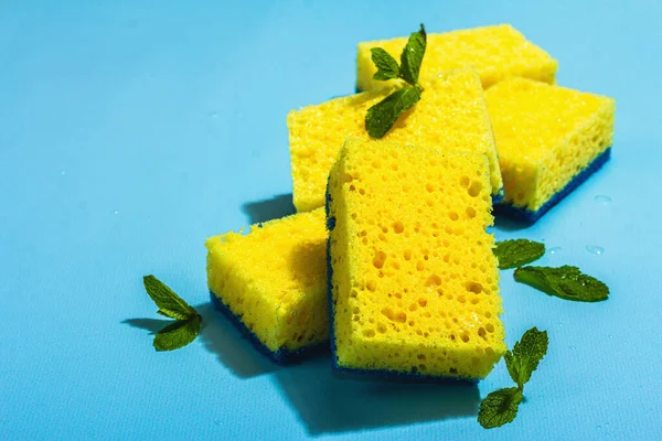 Bright yellow sponges for washing dishes. Organic cleaning concept, minty freshness. A trendy hard light, dark shadow, blue background, flat lay, copy space