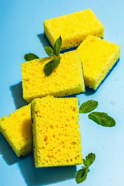 Bright yellow sponges for washing dishes. Organic cleaning concept, minty freshness. A trendy hard light, dark shadow, blue background, flat lay, close up