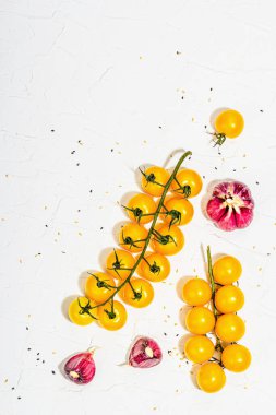 Culinary background with ripe vegetables. Yellow tomato cherries, garlic and sesame seeds. Fresh vegetables on white putty background, modern hard light, dark shadow, flat lay, top view