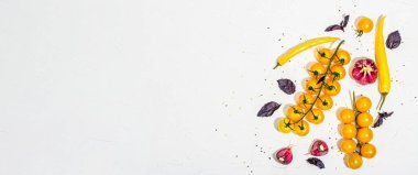 Culinary background with ripe vegetables. Yellow tomato cherries, chili pepper, garlic, purple basil. Fresh vegetables on white putty background, modern hard light, dark shadow, flat lay, banner