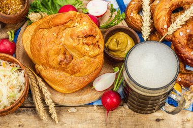 Traditional Oktoberfest set. Pretzels, beer, weisswurst, smoked pork knuckle eisbein with fermented cabbage and mustard. German festival food concept. Old wooden background, top view