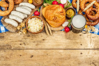 Traditional Oktoberfest set. Pretzels, beer, weisswurst, smoked pork knuckle eisbein with fermented cabbage and mustard. German festival food concept. Old wooden background, top view
