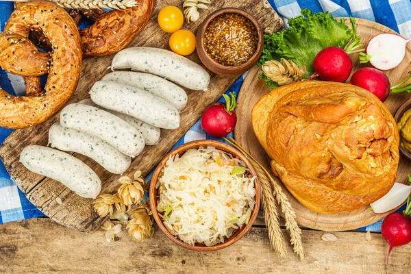 Traditional Oktoberfest set. Pretzels, beer, weisswurst, smoked pork knuckle eisbein with fermented cabbage and mustard. German festival food concept. Old wooden background, top view