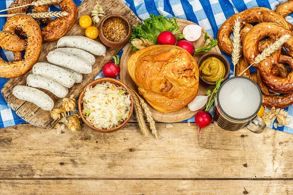 Traditional Oktoberfest set. Pretzels, beer, weisswurst, smoked pork knuckle eisbein with fermented cabbage and mustard. German festival food concept. Old wooden background, top view
