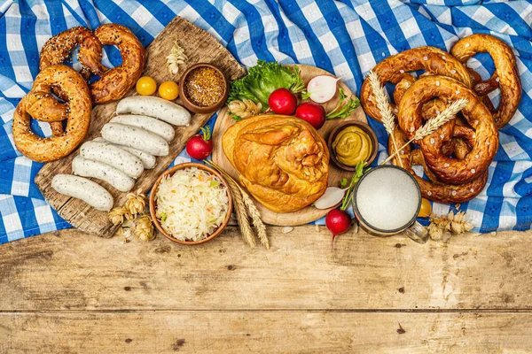 Traditional Oktoberfest set. Pretzels, beer, weisswurst, smoked pork knuckle eisbein with fermented cabbage and mustard. German festival food concept. Old wooden background, top view