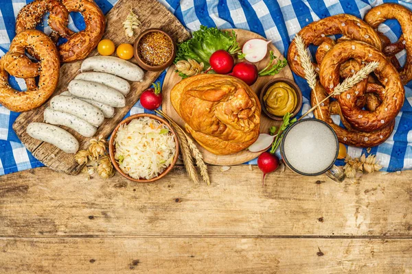 Traditional Oktoberfest set. Pretzels, beer, weisswurst, smoked pork knuckle eisbein with fermented cabbage and mustard. German festival food concept. Old wooden background, top view