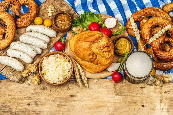 Traditional Oktoberfest set. Pretzels, beer, weisswurst, smoked pork knuckle eisbein with fermented cabbage and mustard. German festival food concept. Old wooden background, top view