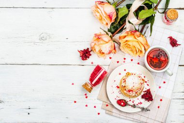 Romantik çay kavramı. Fransız Shu keki, amber çayı, bir buket gül, şenlikli dekor. Sevgililer Günü konsepti, Kadınlar Günü 8 Mart, Düğün. Beyaz tahta arkaplan, üst görünüm