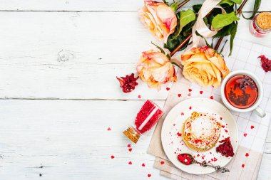 Romantik çay kavramı. Fransız Shu keki, amber çayı, bir buket gül, şenlikli dekor. Sevgililer Günü konsepti, Kadınlar Günü 8 Mart, Düğün. Beyaz tahta arkaplan, üst görünüm