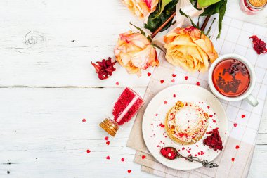 Romantik çay kavramı. Fransız Shu keki, amber çayı, bir buket gül, şenlikli dekor. Sevgililer Günü konsepti, Kadınlar Günü 8 Mart, Düğün. Beyaz tahta arkaplan, üst görünüm