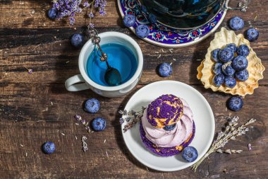 Romantik çay kavramı. Fransız Shu keki, lavanta çayı, yabanmersini, şenlikli dekor. Sevgililer Günü konsepti, Kadınlar Günü 8 Mart, Düğün. Sert ışık, karanlık gölge, ahşap arka plan, üst manzara