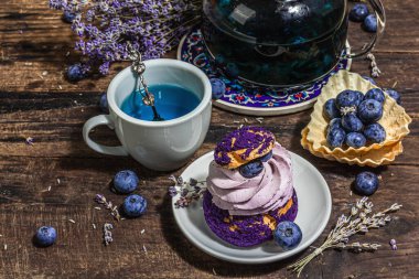 Romantik çay kavramı. Fransız Shu keki, lavanta çayı, yabanmersini, şenlikli dekor. Sevgililer Günü konsepti, Kadınlar Günü 8 Mart, Düğün. Sert ışık, karanlık gölge, ahşap arka plan, kapat