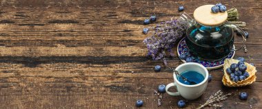 Kır çayı konsepti. Lavanta çiçekleri ve yabanmersini. Vintage düzenleme, sert ışık, koyu gölge, ahşap arkaplan, afiş biçimi