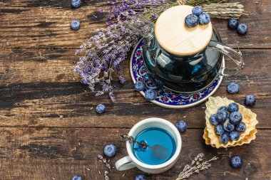 Kır çayı konsepti. Lavanta çiçekleri ve yabanmersini. Vintage düzenleme, sert ışık, karanlık gölge, ahşap arka plan, üst görünüm