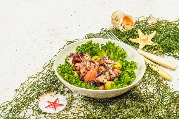 Octopus salad with lettuce, olives and spices in a bowl. Fresh and healthy seafood, marine decor. Trendy hard light, dark shadow, plaster background